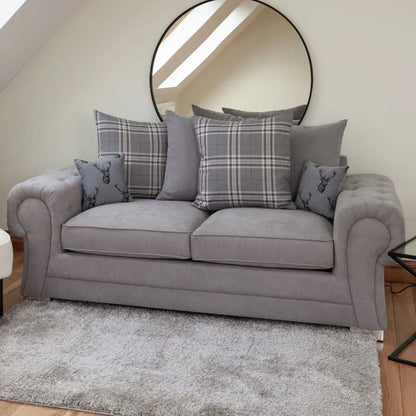 Gray sofa with plaid and gray cushions in a room with a round mirror on the wall.