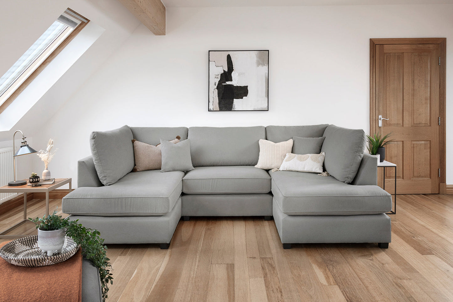 Gray sectional sofa in a modern living room with wooden floor and white walls.